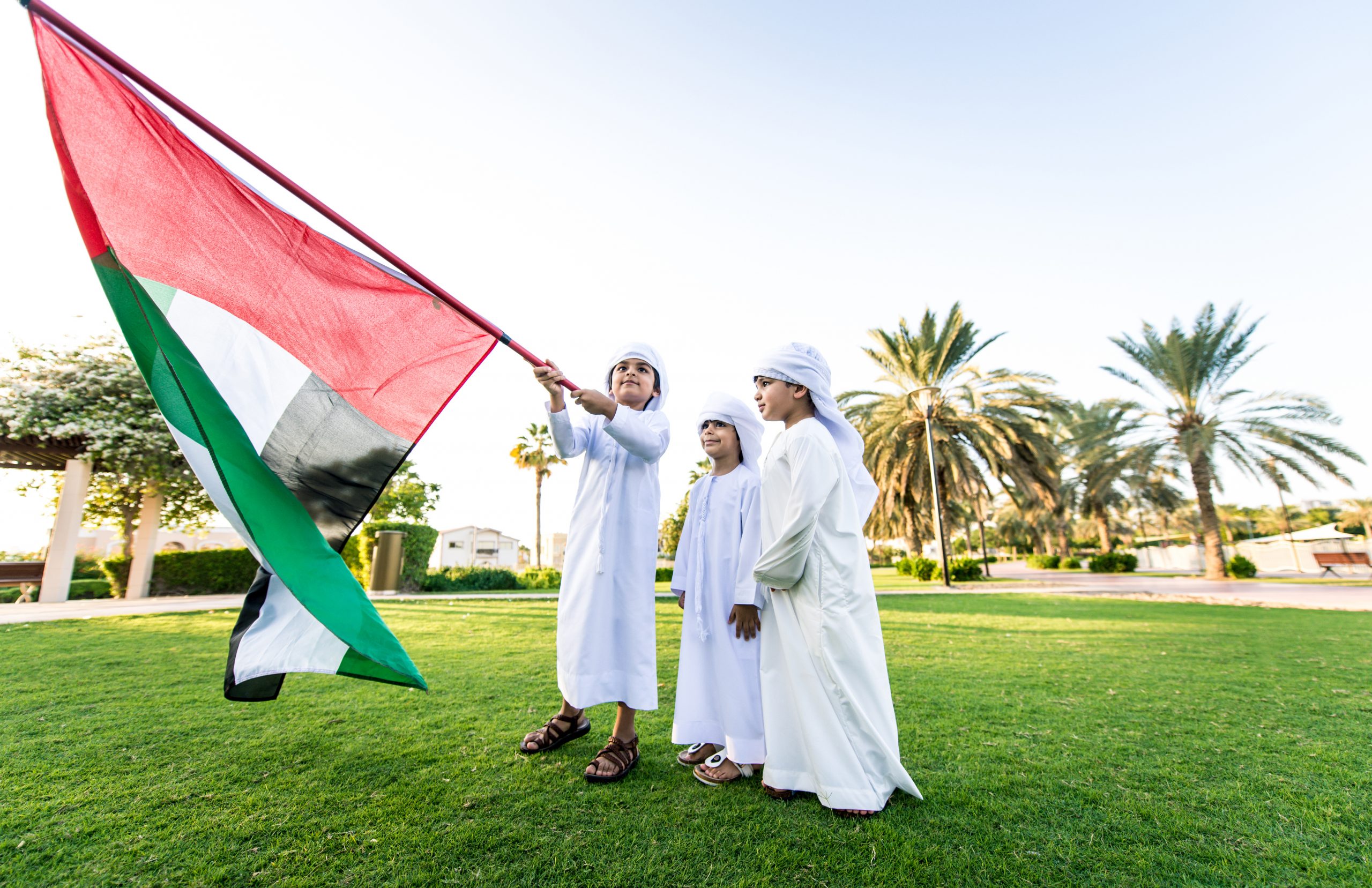 Children playing together in Dubai in the park. Group of kids wearing traditional kandura white dress from arab emirates